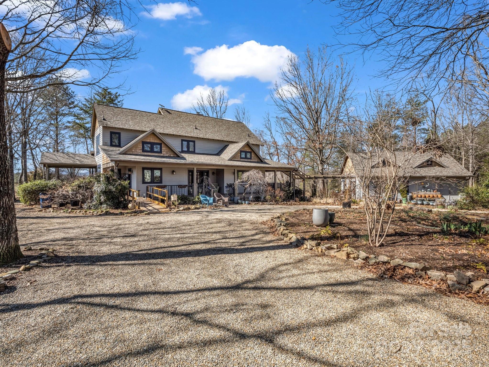 Two-story home with a covered porch, detached outbuilding, and broad gravel driveway.