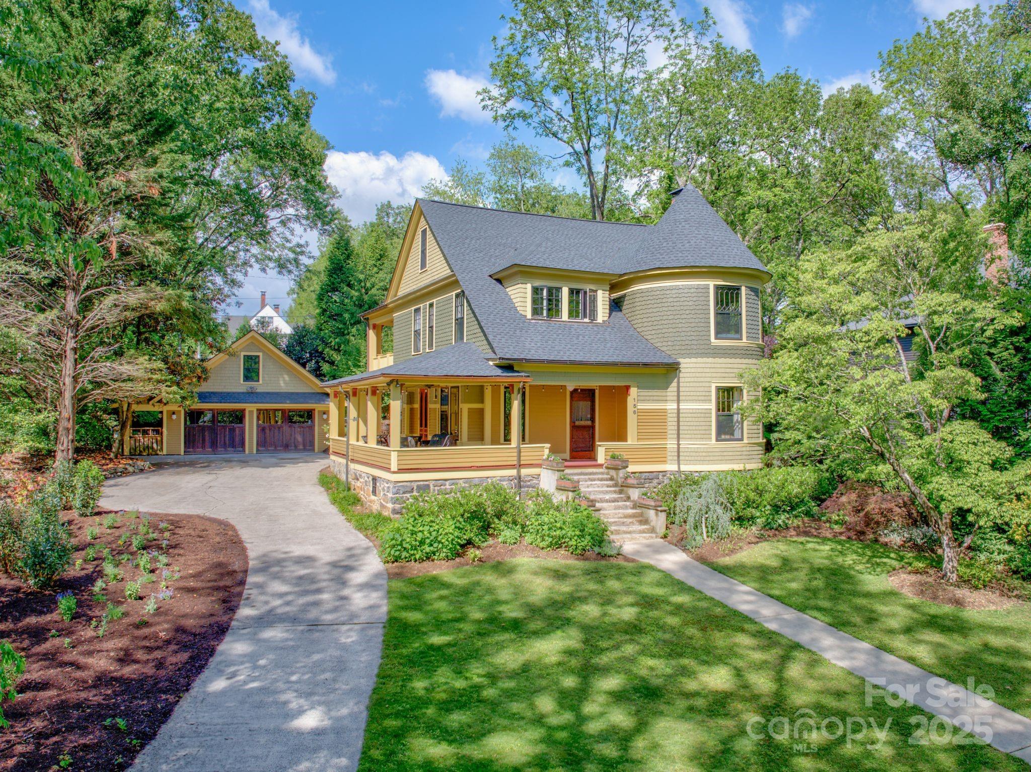 Two-story house with a round turret, wraparound porch, detached garage, and landscaped grounds.