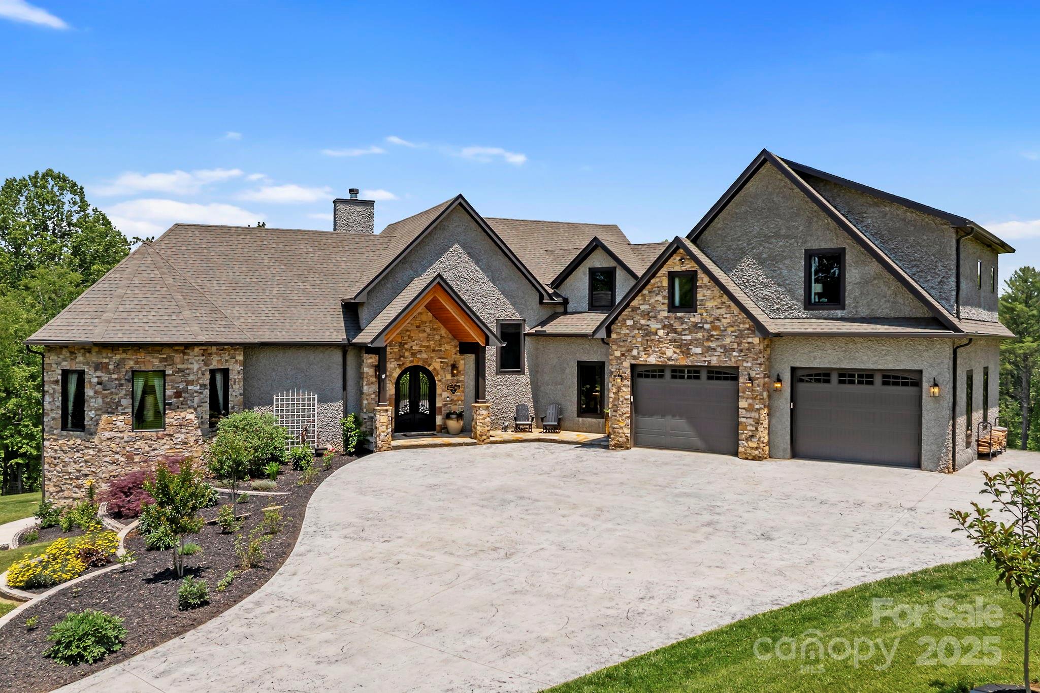Two-story stone-and-stucco home with a curved driveway, landscaped garden, and two-car garage.
