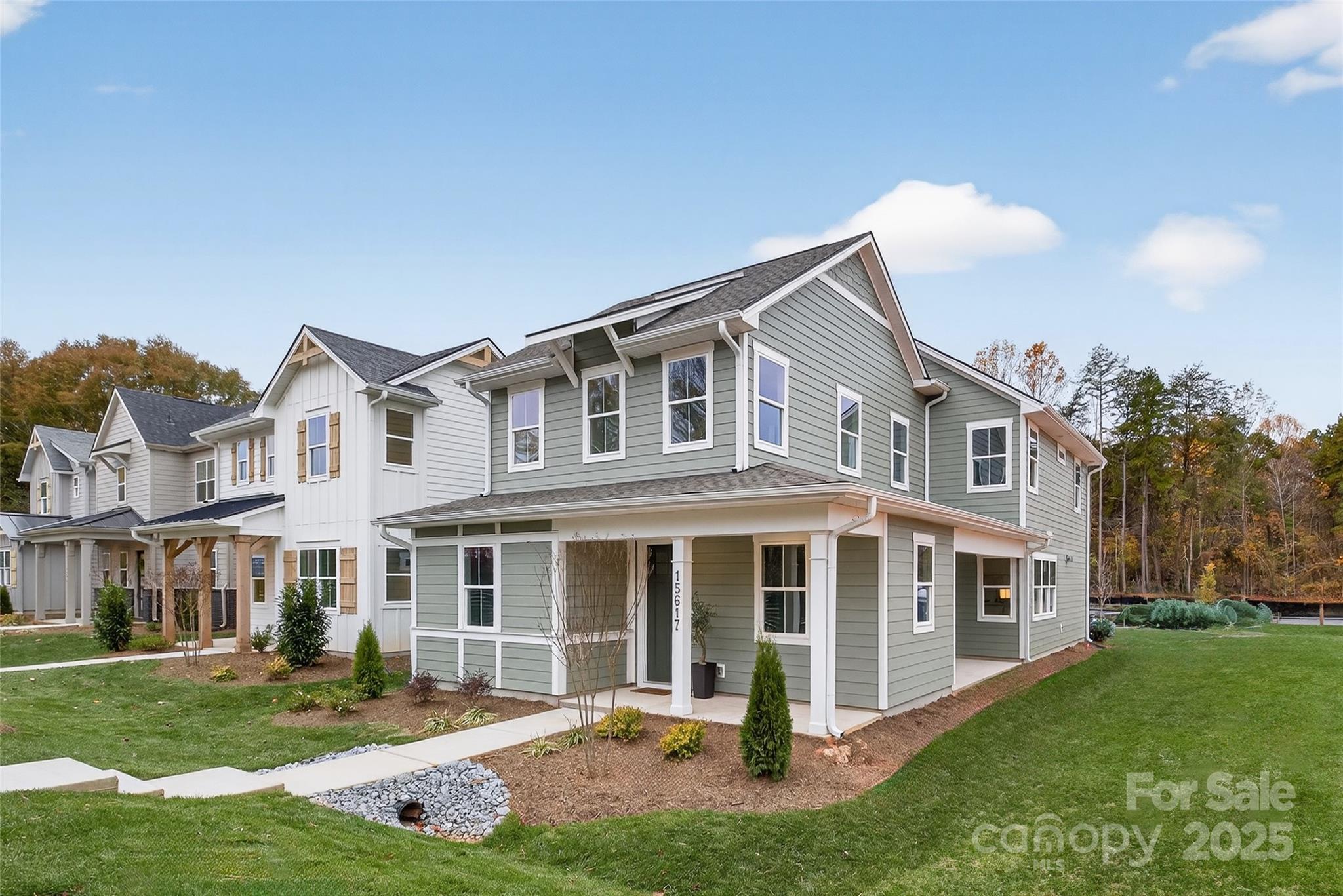 Gray-green two-story home with white trim and a covered porch, beside neighboring homes.