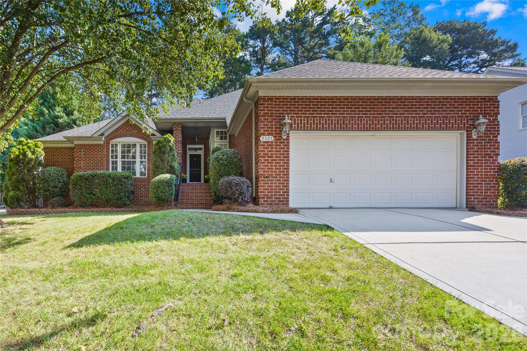 Red brick home with a white double garage door, landscaped front yard, and concrete driveway.