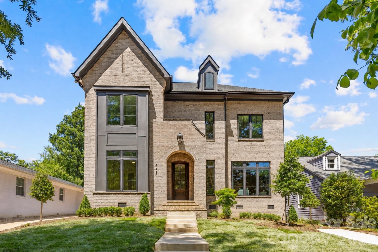 Two-story light brick house with a steep gable, arched entry, and landscaped front lawn.