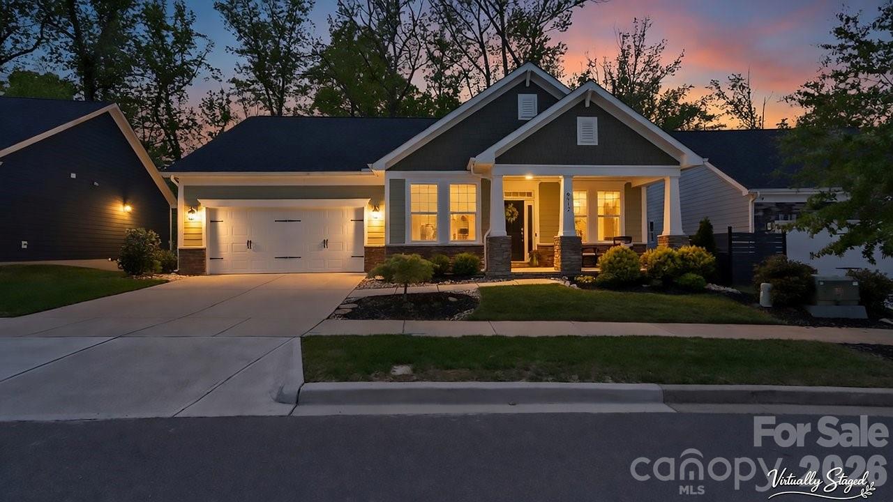 Single-story house at dusk with a two-car garage, covered porch, and warmly lit windows.