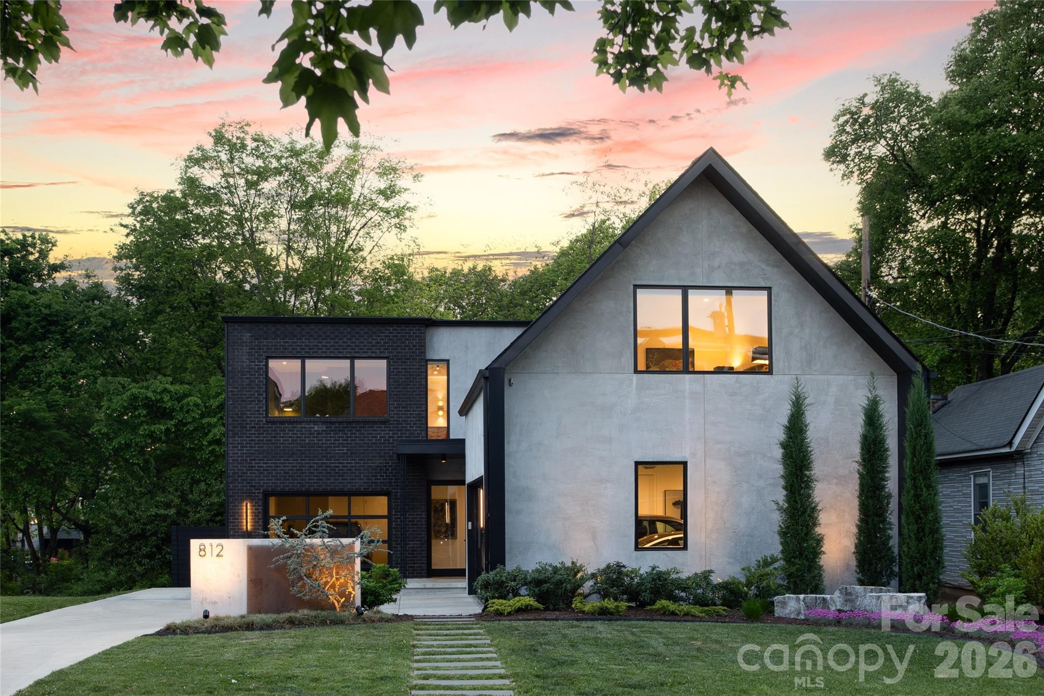 Modern two-story home with a steep triangular roof and illuminated windows at dusk.
