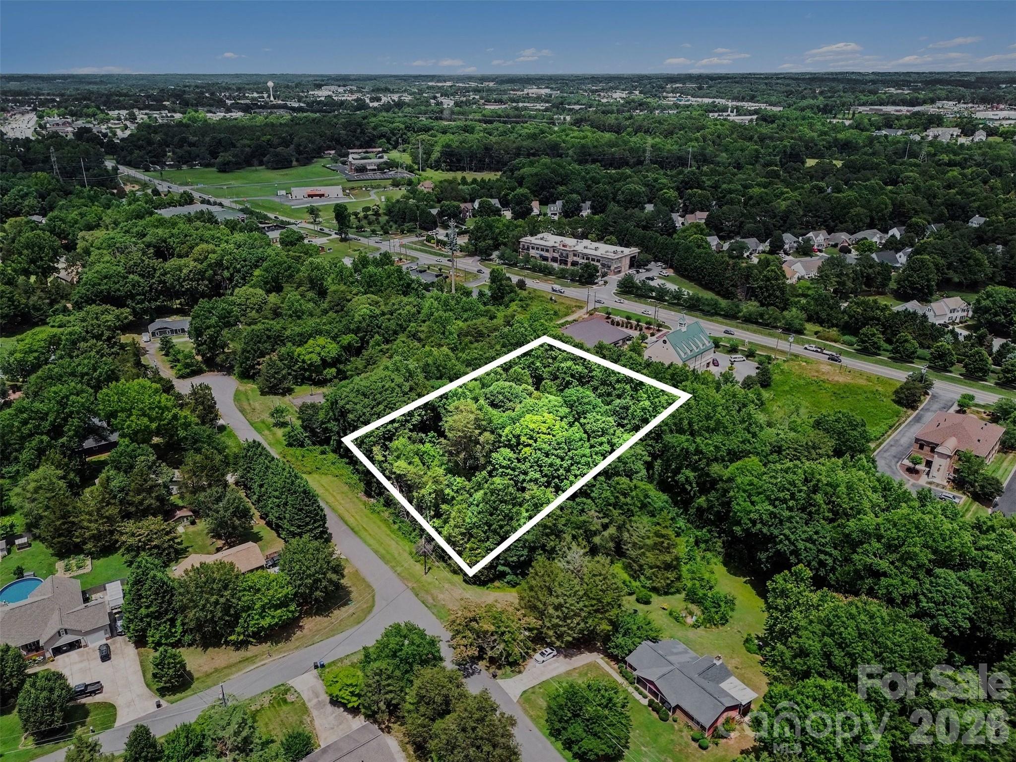 Aerial view of a wooded lot outlined in white among homes and roads.