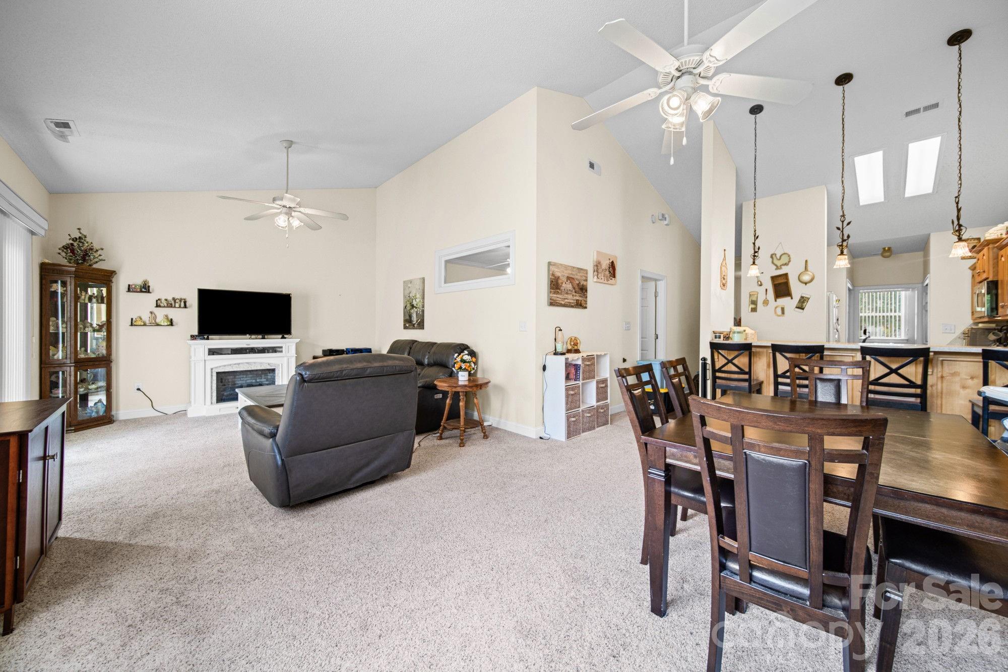 Open-plan living and dining room with vaulted ceilings, leather seating, fireplace, and wooden dining table.