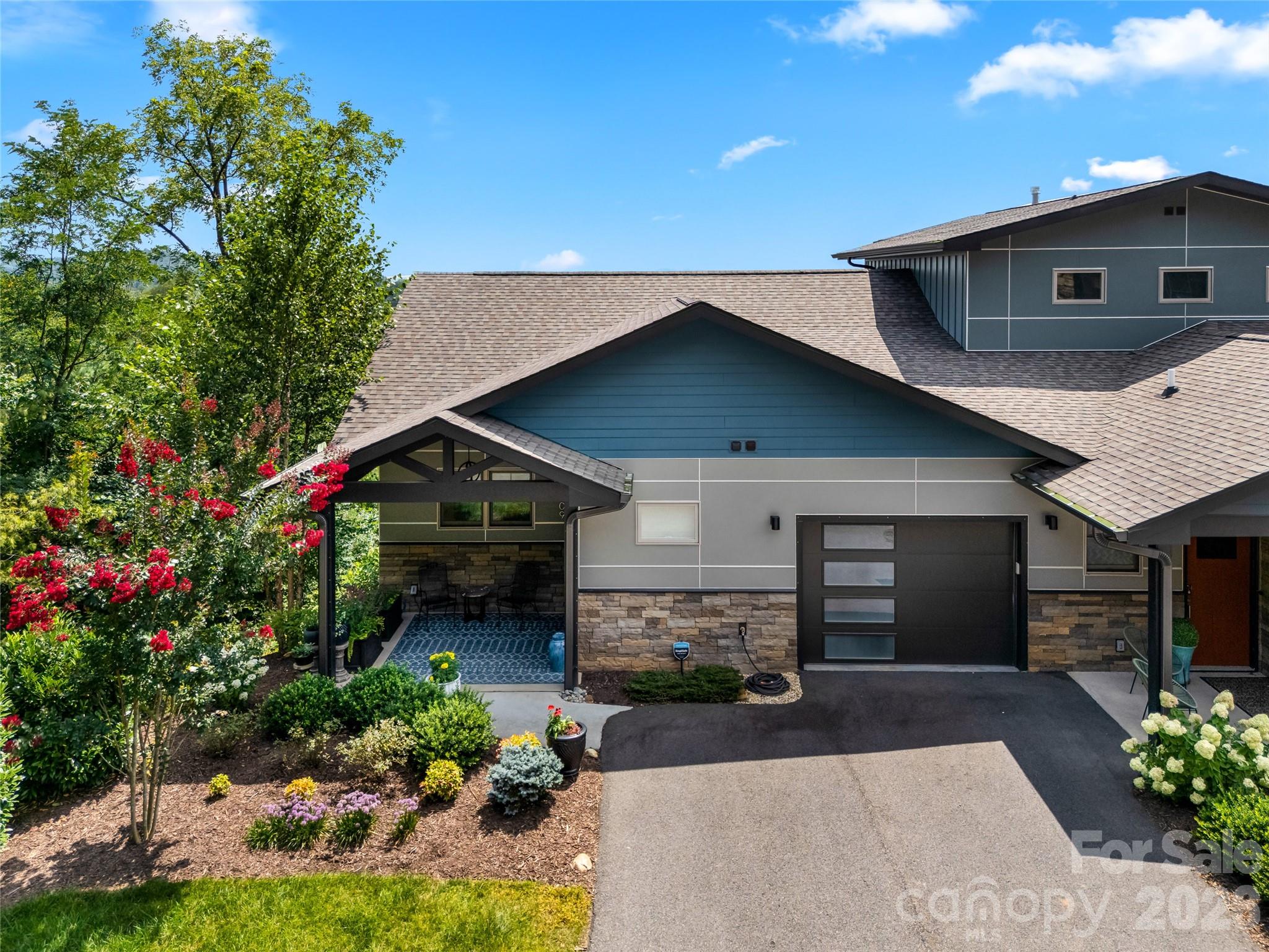 Modern gray-and-blue home with stone accents, a covered patio, and colorful landscaped gardens.