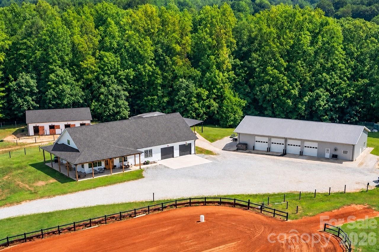 Aerial view of an equestrian property with barns, a riding arena, and surrounding woodland.