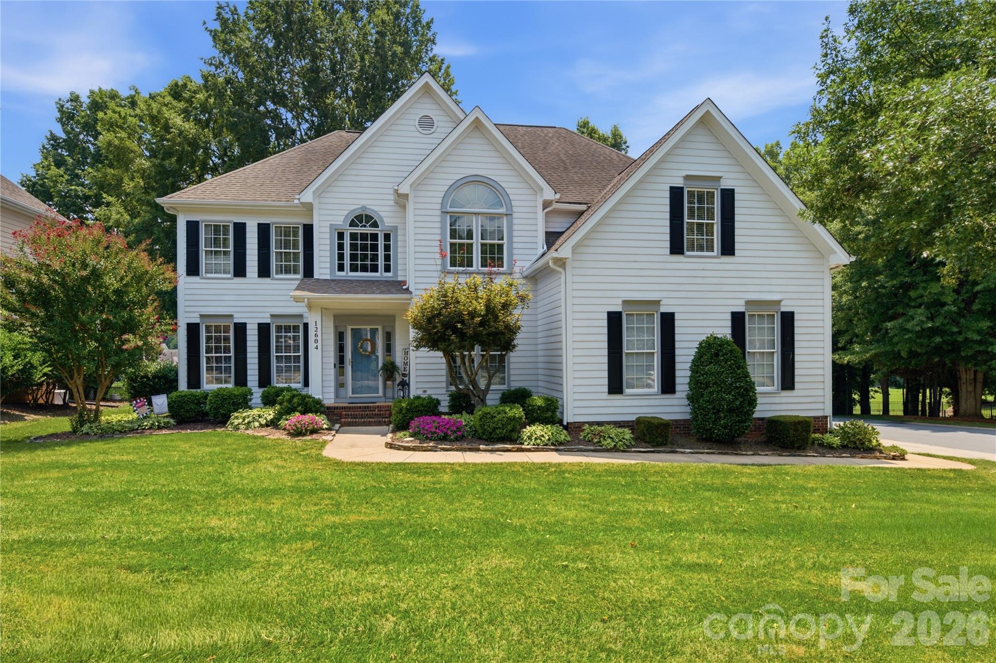 White two-story house with black shutters, a blue front door, and landscaped front lawn.