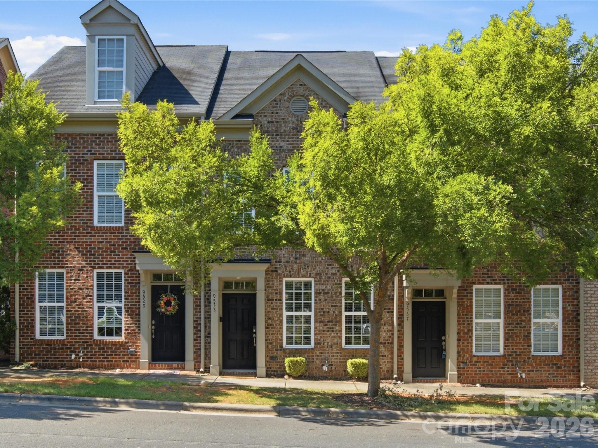 Brick townhomes with dark entry doors and mature trees lining the sidewalk.