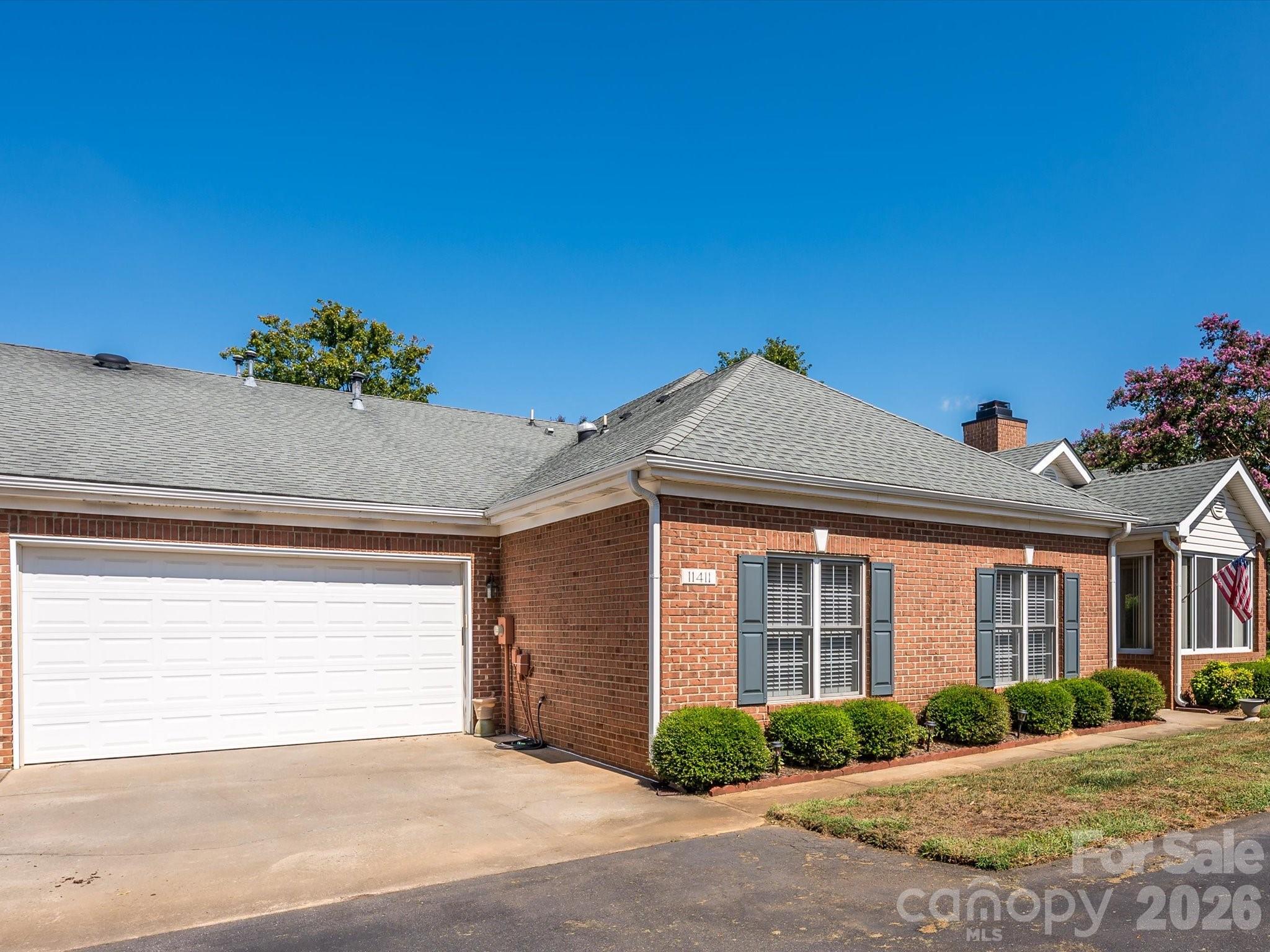 Red brick home with a double garage, gray roof, shuttered windows, and an American flag.