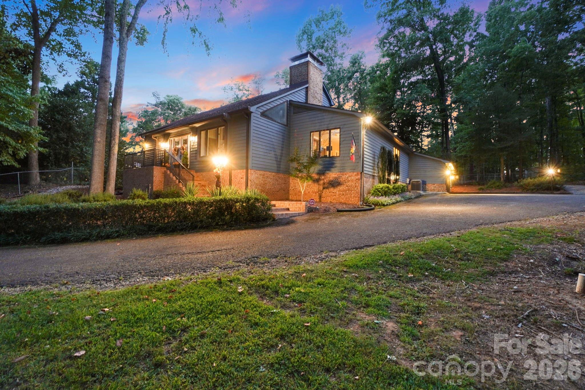 Gray-sided, brick-front home with a raised deck and glowing exterior lights at dusk.