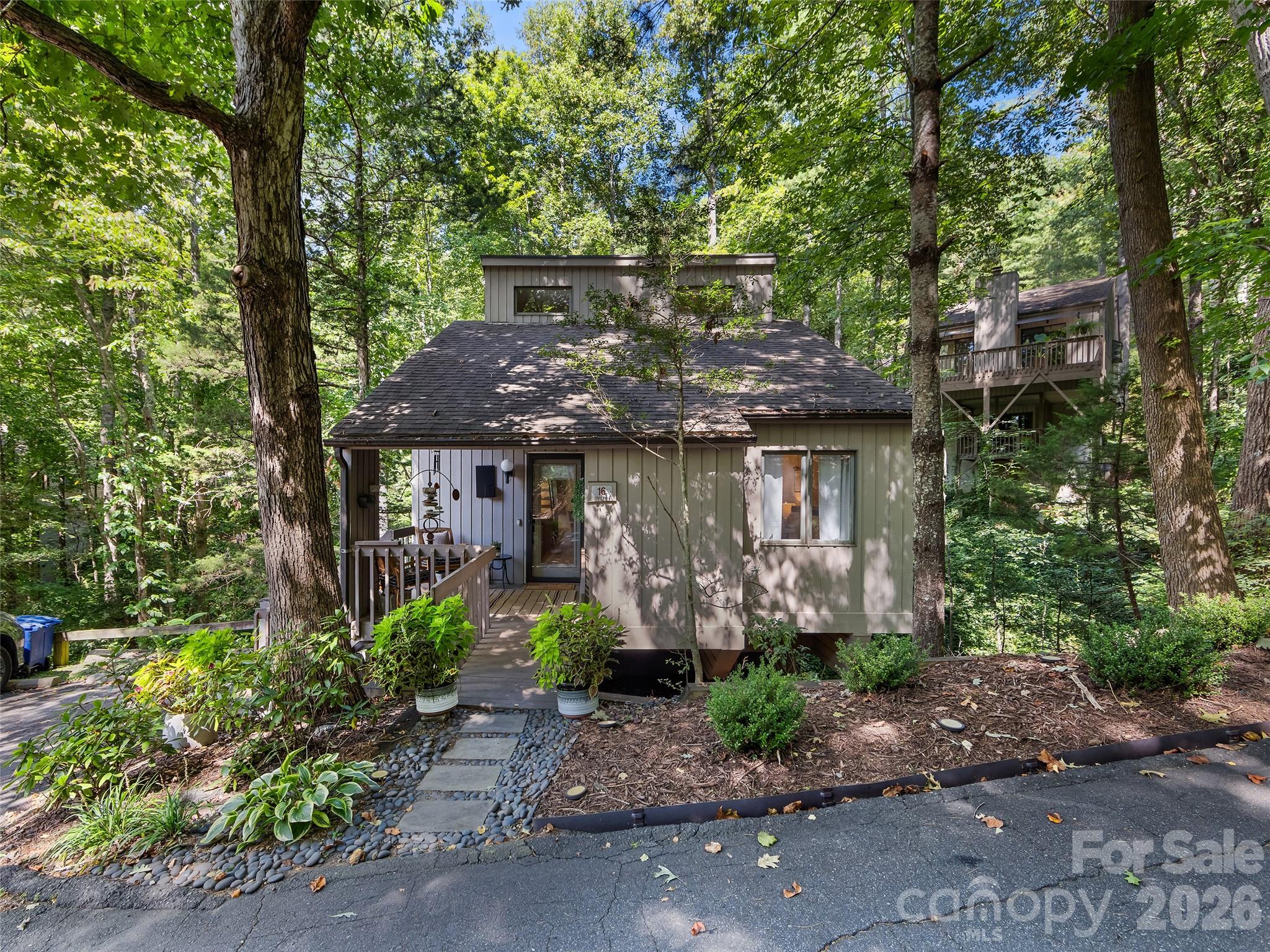 Gray two-story home nestled among mature trees, with a stone path and raised deck.