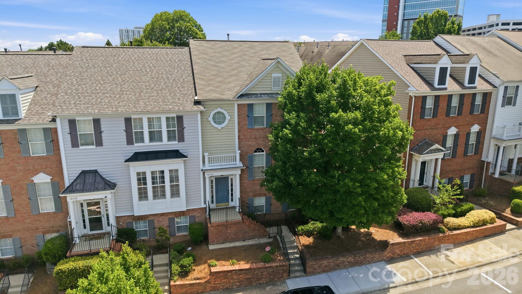 Row of attached townhomes with brick facades, landscaped fronts, and a large shade tree.
